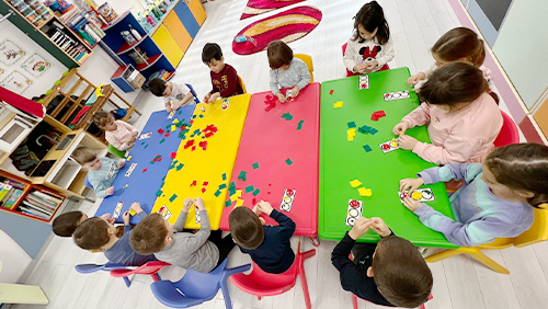Copiii lucrează cu forme colorate la mesele din sala de grupă.